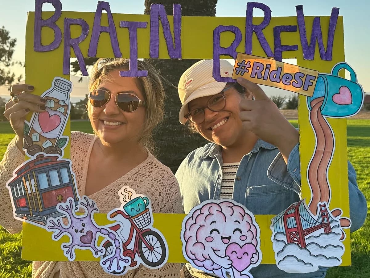 Two people smiling through the handmade Brain Brew photo frame