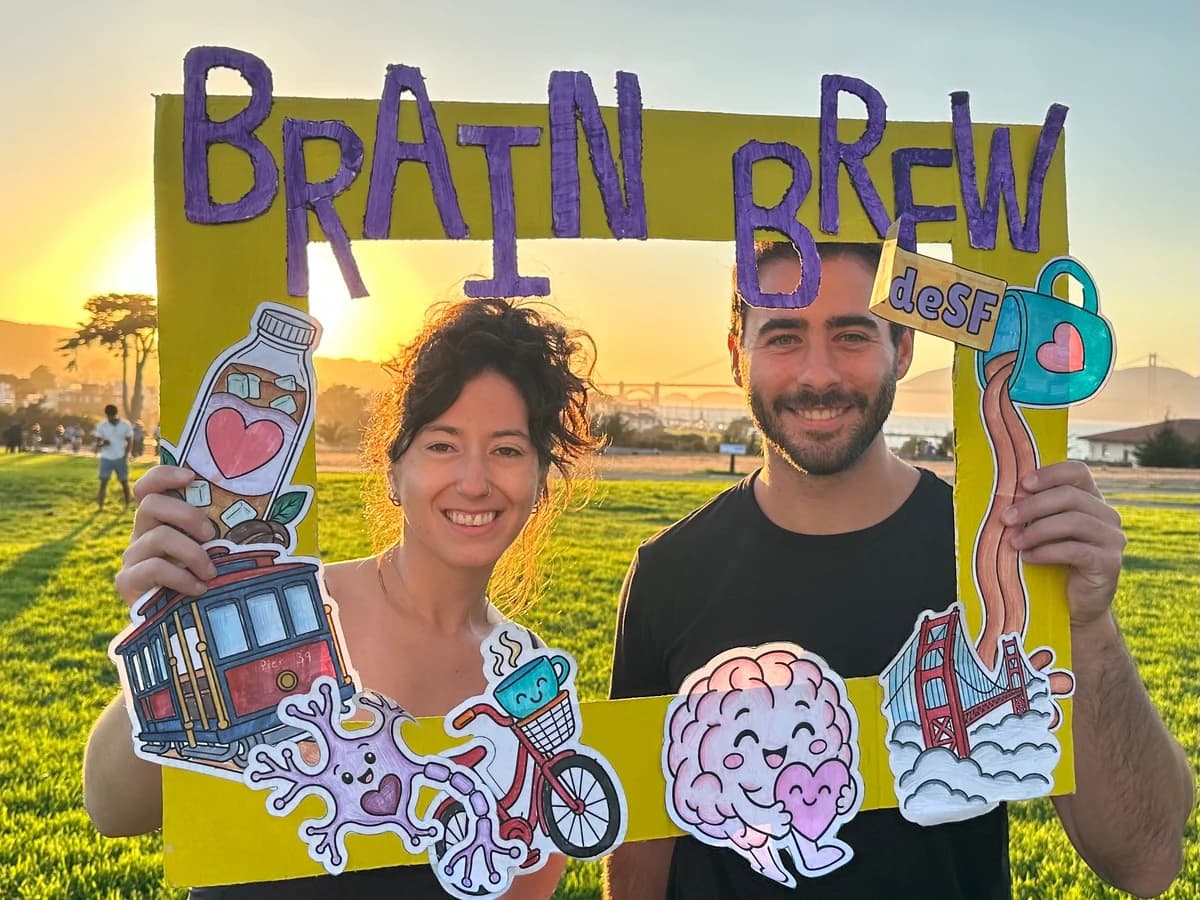 Two people holding the Brain Brew photo frame at golden hour